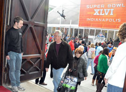 As a zip line rider zooms over thousands of pedestrians filling Capitol Avenue, Keith Echternach, left, a member of St. John the Evangelist Parish in Indianapolis, welcomes Super Bowl visitors into his parish’s historic church on Feb. 3. (Photo by Sean Gallagher)