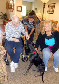 Joe Bocard, a resident of the Villas at Guerin Woods in Georgetown, feeds a treat to Joe, a mixed-breed hound, as Jennifer Nalley, human resources manager, and Judy Foster, who runs a small-breed rescue program in Kentucky and southern Indiana, watch him make friends with the dog. (Photo by Patricia Happel Cornwell)
