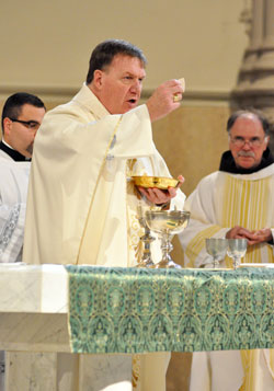Archbishop Joseph W. Tobin elevates the Eucharist during an Oct. 20 Mass at St. John the Evangelist Church in Indianapolis. Concelebrating at the Mass was, at right, Franciscan Father Larry Janezic, pastor of Sacred Heart of Jesus Parish in Indianapolis. Ford Cox, executive assistant to the archbishop and liaison for episcopal affairs, left, assisted at the liturgy. (Photo by Sean Gallagher)