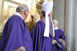 Archbishop Joseph W. Tobin, center, ritually knocks on a door of SS. Peter and Paul Cathedral in Indianapolis prior to the start of the Dec. 2 Evening Prayer liturgy that welcomed him as the sixth archbishop of Indianapolis. Accompanying him are Deacons Wayne Davis, left, and Francis Klauder. (Photo by Sean Gallagher)