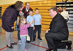 Archbishop Joseph W. Tobin reacts to 3-year-old Kathryn Mack showing him her age during a Feb. 19 reception at St. Louis Parish in Batesville following a Mass celebrated there by the archbishop for Catholics in the Batesville Deanery. Joining Kathryn in meeting the archbishop are members of her family, from left: Deb, Grace (partially obscured), Pete, Christian and Spencer Mack, all members of St. Louis Parish. (Photo by Sean Gallagher)