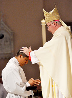 Bishop Christopher J. Coyne ritually lays hands on then-transitional deacon candidate Martin Rodriguez on June 23, 2012, at SS. Peter and Paul Cathedral in Indianapolis. Deacon Rodriguez, a member of St. Mary Parish in Indianapolis, will be ordained a priest on May 18. (File photo by Mary Ann Garber)