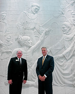 A stunning relief sculpture of St. Francis of Assisi caring for a leper represents the combination of faith and health care that will drive the new College of Osteopathic Medicine at Marian University in Indianapolis that starts its first day of classes on Aug. 12. Dr. Paul Evans, left, dean of the medical school, and Daniel Elsener, president of the university, pose in front of the relief sculpture. (Photo by John Shaughnessy)