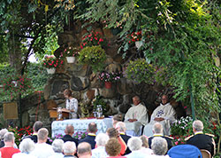Ann Decker, left, proclaims the first reading as Deacon Robert Decker and Franciscan Father Humbert Moster listen in the grotto of St. Mary-of-the-Rock Parish in Franklin County on Aug. 15. For 90 years, the parish has celebrated a Feast of the Assumption tradition of Mass in the grotto followed by a rosary procession with the Eucharist and a statue of Mary. The procession ends in the church for adoration, songs and Benediction. (Photo by Natalie Hoefer)
