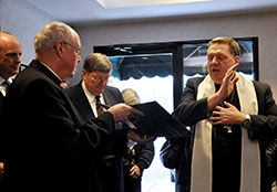Archbishop Joseph W. Tobin blesses the people and studios at Catholic Radio Indy’s new offices on Dec. 17, while Msgr. Joseph Schaedel, pastor of St. Luke the Evangelist Parish in Indianapolis, holds the prayer book, and Catholic Radio Indy founder and chairman Bob Teipen, middle, bows his head in prayer. 