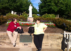 Catechists Mary Wagner, left, of St. Michael the Archangel Parish in Indianapolis, and Lynell Chamberlain of St. Joseph Parish in Clark County pause for a conversation near the statue of Saint Francis of Assisi on July 15 on the campus of Franciscan University of Steubenville in Steubenville, Ohio. Wagner and Chamberlain were attending the St. John Bosco Conference for Catechists and Religious Educators offered every summer at the university.  (Submitted photo)