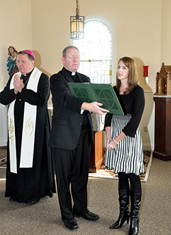 Archbishop Joseph W. Tobin listens as Sarah Bardol, director of the new Women’s Care Center in Indianapolis, reads in the chapel during a service to bless the facility on Nov. 19. Father Patrick Beidelman, executive director of the archdiocesan Secretariat for Spiritual Life and Worship, holds a book for Bardol. (Photo by Natalie Hoefer)