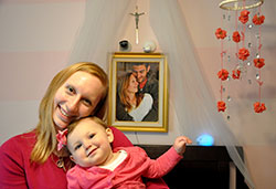 Jennifer Trapuzzano snuggles with her daughter Cecilia in the bedroom where Cecilia sleeps in a crib beneath a crucifix and a photo of her parents. Cecilia was born on April 25, 2014—24 days after her father Nathan Trapuzzano was shot and killed during a robbery as he took a walk through their Indianapolis neighborhood. (Photo by John Shaughnessy)