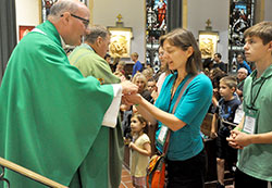 Msgr. William Stumpf, archdiocesan vicar general, gives Communion to Samantha McGuire, a member of St. Martin of Tours Parish in Martinsville, during a Sept. 25 Mass in the upper church of St. John the Evangelist Church in Philadelphia. Preparing to receive Communion next is McGuire’s son, Joseph. They were among 46 Catholics from central and southern Indiana who participated in the World Meeting of Families in Philadelphia from Sept. 22-25. (Photo by Sean Gallagher)