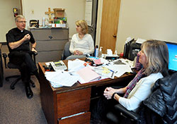 Msgr. Paul Koetter, left, pastor of Holy Spirit Parish in Indianapolis, speaks on Feb. 25 with Kathy Peacock and Suzanne McLaughlin, the parish’s business managers, in the office of the Indianapolis East Deanery faith community. A $1 million grant recently awarded to the Archdiocese of Indianapolis by Lilly Endowment Inc. will help pastoral leaders in central and southern Indiana nurture their management skills and financial knowledge. (Photo by Sean Gallagher)