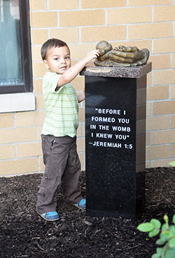 Nicholas Lam, a member of St. Luke the Evangelist Parish in Indianapolis, touches the head of the sculptured infant atop the new Memorial to the Unborn at St. Matthew the Apostle Parish in Indianapolis on May 1. (Photo by Natalie Hoefer)