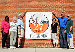Volunteers for the Indianapolis council of the Society of St. Vincent de Paul stand with a “Mission 27 Resale Coming Soon” sign on July 11 outside of the thrift store’s soon-to-be home at 1201 E. Maryland St. in Indianapolis. The volunteers are Changing Lives Forever director Domini Rouse, left, distribution intake manager Barbara Niezgodski, president John Ryan, linens and bedding coordinator Kathleen Williams, distribution center executive director Jeff Blackwell and south district council president Charlie Mazza. (Photo by Natalie Hoefer)