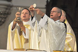 Father Rick Nagel, left, and Bishop Paul D. Etienne of Cheyenne, Wyo., elevate the Eucharist during an Oct. 31, 2015, Mass at St. John the Evangelist Church in Indianapolis during the Indiana Catholic Men’s Conference. On Oct. 4, it was announced that Pope Francis has named Bishop Etienne as the fourth archbishop of Anchorage, Alaska. (Criterion file photo by Sean Gallagher)