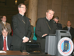Then-Archbishop Daniel M. Buechlein, right, speaks during a Feb. 9, 2011, ceremony at the Indiana Statehouse in Indianapolis during which he, Bishop Timothy L. Doherty of Lafayette, center, Indiana Attorney General Greg Zoeller, left, and other state religious, government and business leaders signed the Indiana Compact, an agreement that calls for immigration reform to happen at the federal and not the state level. Immigration continues to be an issue of great importance to the Church in Indiana. (Criterion file photo by Charles Schisla)