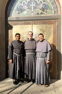 Conventual Franciscan Fathers Savio Manavalan and Mark Weaver and Conventual Franciscan transitional Deacon Mario Serrano stand in front of the doors of St. Joseph University Parish in Terre Haute, where all three serve. (Submitted photo)