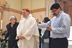 Deacon candidate Juan Carlos Ramirez, right, recites from a prayer card as he, Marie Tobin, left, Domini Rouse and Benedictine Sister Jennifer Mechtild Horner lay their hands upon and pray for Cardinal Joseph W. Tobin in front of the altar at SS. Peter and Paul Cathedral in Indianapolis as part of a prayer and blessing of him during the cardinal’s farewell Mass on Dec. 3. (Photo by Natalie Hoefer)