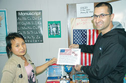 Since arriving in the United States a year ago after being granted political asylum, Ahmed Al-Darraji, right, of Iraq has embraced American life so much that he teaches a Catholic Charities Indianapolis class that helps refugees and immigrants pursue their dream of becoming American citizens. Here, he poses with Zing Tial, a Burmese refugee, as they hold a copy of “The Star Spangled Banner.” (Photo by John Shaughnessy)