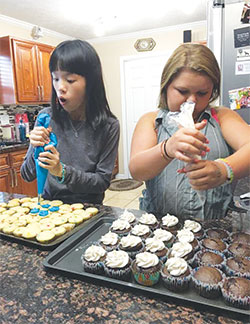 Yiwen Cao, left, and Sara Matthews, a seventh-grader at Seton Catholic High School in Richmond, decorate cupcakes in Sara’s home at the start of the 2016-17 academic year. Yiwen was part of a group of Chinese students who visited Seton for about a month. (Submitted photo)