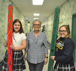 Our Lady of Lourdes middle school teacher Angie Therber and Lourdes eighth-grade students Grace Swinefurth, left, and Olivia Wilson show the “peace posts” created by the Indianapolis school’s eighth graders to promote peace in the school’s east side neighborhood. (Photo by Sean Gallagher)