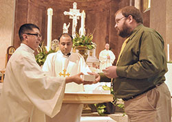 Then-transitional Deacon Nicolás Ajpacajá gives holy oils to Adam Welp, a member of Holy Family Parish in New Albany, during the archdiocesan chrism Mass on March 22, 2016, in SS. Peter and Paul Cathedral in Indianapolis. Assisting Deacon Ajpacajá is then-transitional Deacon Meril Sahayam of the Palayamkottai, India, Diocese. (File photo by Sean Gallagher)