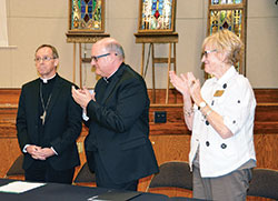 Msgr. William F. Stumpf, archdiocesan administrator, center, and archdiocesan chancellor Annette “Mickey” Lentz applaud Archbishop-designate Charles C. Thompson after his press conference in the Archbishop Edward T. O’Meara Catholic Center in Indianapolis on June 13. (Photo by Natalie Hoefer)