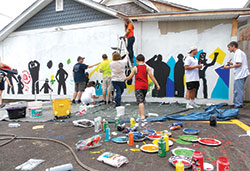 The students of the Missionary Disciples Institute get hands-on service experience helping local children paint a mural on the DAT House, an Indianapolis community center, on June 15. The immersion experience was offered by Marian University in Indianapolis. (Photo by Katie Rutter)