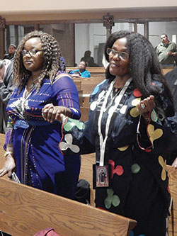 Amaka Ogbuehi, left, and her sister, Nneka Jemie, both natives of Nigeria, hold hands while praying the Lord’s Prayer during the Nov. 3 Mass. (Photo by Mike Krokos)