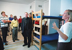 Emily Able, right, director of community and youth services at the archdiocesan Holy Family Shelter in Indianapolis, guides Archbishop Daniel M. Buechlein, center, archdiocesan vocations director Father Eric Johnson, standing behind the archbishop, and a group of archdiocesan seminarians on an Aug. 11, 2010, tour of the shelter for homeless families. (File photo by Sean Gallagher)