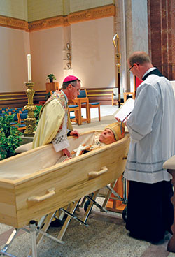 Archbishop Charles C. Thompson, left, prays over the body of Archbishop Emeritus Daniel M. Buechlein during the Rite of Reception on Jan. 30 in SS. Peter and Paul Cathedral in Indianapolis. Father Patrick Beidelman, executive director of the Secretariat for Worship and Evangelization and rector of the cathedral, assists. During the Rite of Reception, the body of Archbishop Buechlein was prayed over and blessed with holy water, and a cross and breviary were placed in the casket. (Photo by Natalie Hoefer)