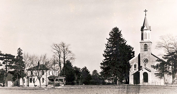 This photo shows the original church and rectory of the former St. Mary Magdalene Parish in Ripley County. The original grounds of the parish were located within what later became the Jefferson Proving Ground, a munitions testing facility operated by the U.S. Army. The land for the proving ground was selected in December 1940. St. Mary Magdalene and several other churches that were located within the proving ground were forced to close or move. The final Mass in the original church was celebrated on Feb. 16, 1941, by then-Bishop Joseph E. Ritter. The parish was closed for six years before being re-opened in 1947 in New Marion. St. Mary Magdalene Parish was merged in December 2013 with Prince of Peace Parish in Madison as part of the “Connected in the Spirit” planning process.