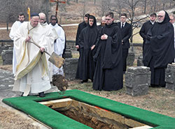 With monks and seminarians looking on, Benedictine Archabbot Kurt Stasiak tosses a spade of dirt onto the casket of Archbishop Emeritus Daniel M. Buechlein on Feb. 1 after it had been lowered into its grave in the cemetery of Saint Meinrad Archabbey in St. Meinrad. (Photo by Sean Gallagher)