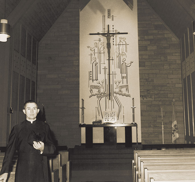 American Martyrs Parish in Scottsburg was founded in 1938, and used a renovated public school as their first church building. In 1963, the parish received funds from the Archdiocesan Home Missions Fund to construct a new church. In this photo, Father William Engbers, pastor, is shown with a mural depicting Christ and the American Martyrs in the new church building, a few days before its dedication on April 19, 1964.
