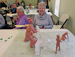At the Cardinal Ritter House annual Irish coffee lecture on March 15, Janice Cooley, right, and Joan Gilley inspect Guy Tedesco’s clay model of a planned lawn sculpture group of Cardinal Joseph E. Ritter and children pulling down a wall symbolic of discrimination. Both are members of Our Lady of Perpetual Help Parish in New Albany. (Photo by Patricia Happel Cornwell)