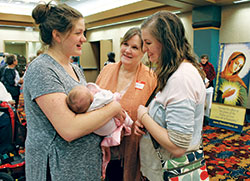 Julie Alumbaugh shows her 2-week-old daughter to her mother Cathy McMahon, center, and twin sister Mary Warren at the Indiana Catholic Women’s Conference on March 10 in Indianapolis. The theme of the conference was “The Sanctification of the Family.” (Photo by Victoria Arthur)