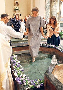 Catechumen Hannah Bach, 18, is guided into the baptismal font at St. Joseph University Church in Terre Haute by Conventual Franciscan Father Mark Weaver, the parish’s pastor, and her sponsor Sierra Flores during the Easter Vigil Mass on March 31. (Submitted photo by Bill Foster)