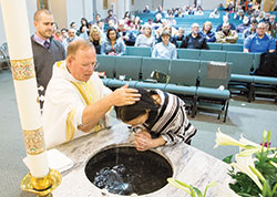 In St. Teresa Benedicta of the Cross Church in Bright, parish pastor Father Randall Summers baptizes Trisha Schwing during the Easter Vigil Mass on March 31 while her sponsor Mark Pinkerton looks on. (Submitted photo) 
