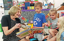 For 44 years, Terry Horton has served as a teacher and an administrator in Catholic schools in the New Albany Deanery. Here, she shares a book and a smile with pre-kindergarten students Liam McGuire, left, Mia Wilkinson and Raegan Schoen. (Submitted photo)
