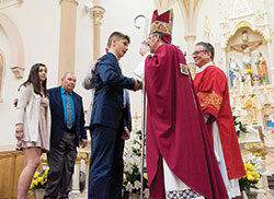 Archbishop Charles C. Thompson shakes hands with Nathan Cullen of St. Teresa Benedicta of the Cross Parish in Bright after conferring upon him the sacrament of confirmation. In the background, fellow parishioner Avery Daniels stands next to her sponsor waiting to receive the sacrament. Archbishop Thompson baptized the youths of St. Teresa Benedicta of the Cross and four other parishes in St. Louis Church in Batesville on April 21. (Submitted photo by Waltz Photography, LLC)
