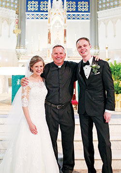 Father Rick Nagel, pastor of St. John the Evangelist Parish in Indianapolis, poses for a photo with Amanda and Craig Schebler after presiding at their wedding at the parish church on July 8, 2017. (Photo courtesy of Soul Creations Photography)