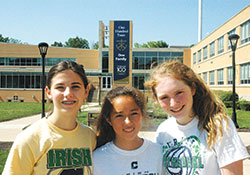 Against the backdrop of a banner saluting the 100th anniversary of Cathedral High School in Indianapolis, freshman volleyball players Ava Yaggi, left, Audrey Gerdts and Abby Rotz are all smiles as they pose for a photo on the campus of the private Catholic school. (Photo by John Shaughnessy)