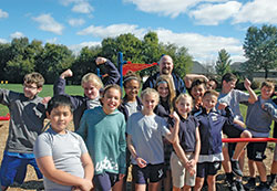 Physical education teacher Steve Imel flashes a smile as members of the sixth-grade class at SS. Francis and Clare of Assisi School in Greenwood strike their best flexing poses on the new fitness area at the school. (Photo by John Shaughnessy)