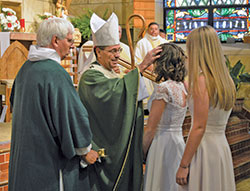Archbishop Charles C. Thompson anoints the head of Lexie Curl during the sacrament of confirmation at St. Mary Church in Lanesville on Oct. 13. He is assisted by Deacon Richard Cooper, left, while Lexie’s sponsor Kaylee Wheatley, right, looks on. The Mass also celebrated the 175th anniversary of the parish’s founding. (Photo by Natalie Hoefer)