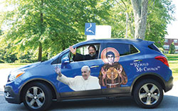Conventual Franciscan Father John Bamman smiles and waves from his 2014 Buick Encore, the vehicle that he drives across the Midwest—with Pope Francis and St. Francis at his side—to promote vocations. (Submitted photo)