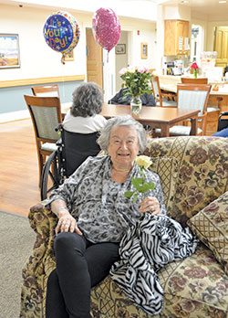 A resident—or elder, as residents are respectfully referred to at Guerin Woods retirement care community—shows off a rose she received as part of a birthday celebration for the elder seated behind her in one of the community’s villas on Oct. 13. (Photo by Natalie Hoefer)