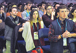 Colleen Tragonski, center, kneels with other young people in prayer on Jan. 6 during a Mass at the SEEK2019 conference that drew 17,000 mainly college students from across the country to the Indiana Convention Center in Indianapolis. “The Holy Spirit is so present here, everywhere in the atmosphere,” Tragonski said. “That’s the best way that I can put it.” (Photo by Sean Gallagher) 