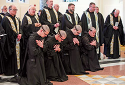 With monks of Saint Meinrad Archabbey standing behind them, Benedictine Brothers Simon Herrmann, left, Nathaniel Szidik, Joel Blaize and Jean Fish kneel in prayer during a Jan. 25 liturgy at the Archabbey Church of Our Lady of Einsiedeln in St. Meinrad in which the brothers professed solemn vows. In a ritual symbolizing humility, monks of Saint Meinrad who profess solemn vows have all of their hair cut off except for a small band that is traditionally called in Latin a “corona” (“crown”). (Photo courtesy of Saint Meinrad Archabbey)