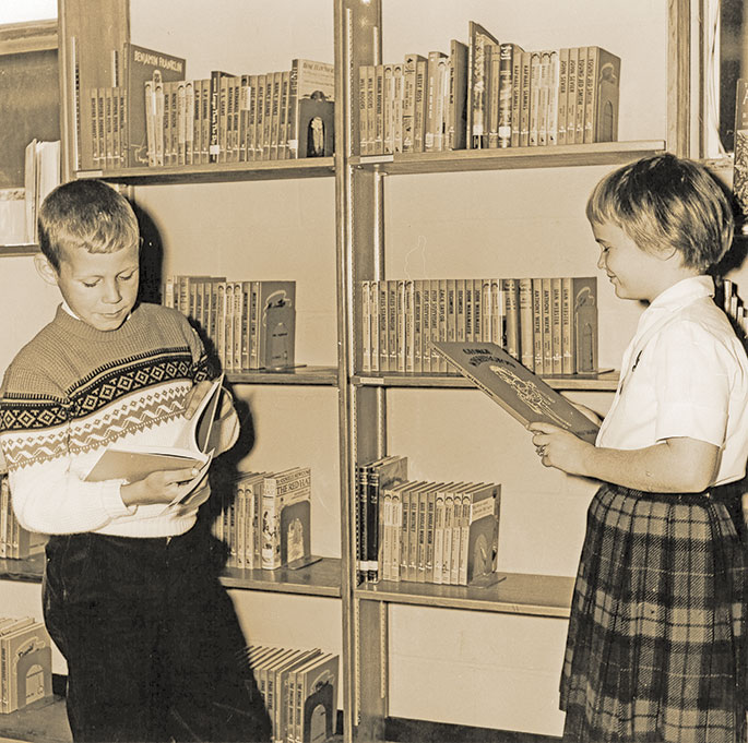 In this photo, Tim Fox and Irma Noel peruse the biography section of the library at the St. Luke the Evangelist School in Indianapolis. The photo was published in the St. Luke the Evangelist Church dedication souvenir booklet from Oct. 22, 1961. The booklet notes that the school library contained 1,200 books at that time. St. Luke Parish was established on Sept. 2 of that same year, and the school, which had already been under construction, opened a few days later.