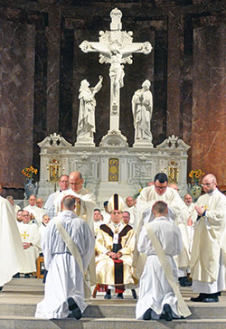 Transitional Deacons Timothy DeCrane, left, and Vincent Gillmore kneel on June 1 in SS. Peter and Paul Cathedral while Father Vincent Lampert ritually lays hands on Deacon DeCrane and Father James Brockmeier ritually lays hands on Deacon Gillmore. (Photo by Sean Gallagher) 