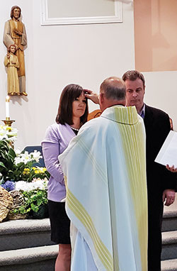 Standing next to her sponsor and husband Doug, Bridget Hornbach is anointed with chrism oil by her pastor, Father Randall Summers, as part of the Rite of Confirmation during the Easter Vigil Mass at St. Teresa Benedicta of the Cross Church in Bright on April 20. (Submitted photo by Larry Strange) 