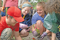Clare Stephens, center, a mentor at the Missionary Disciples Institute hosted by Marian University in Indianapolis, plants flowers outside the Unleavened Bread Café in Indianapolis with Elizabeth Reed, right, a student at St. Louis Catholic High School in Lake Charles, La., on June 20. The activity aimed to help the young people become acquainted with the members of the café, which was founded as a community space for women who had been formerly incarcerated, addicted to drugs, or experienced other difficult circumstances. (Photo by Katie Rutter)